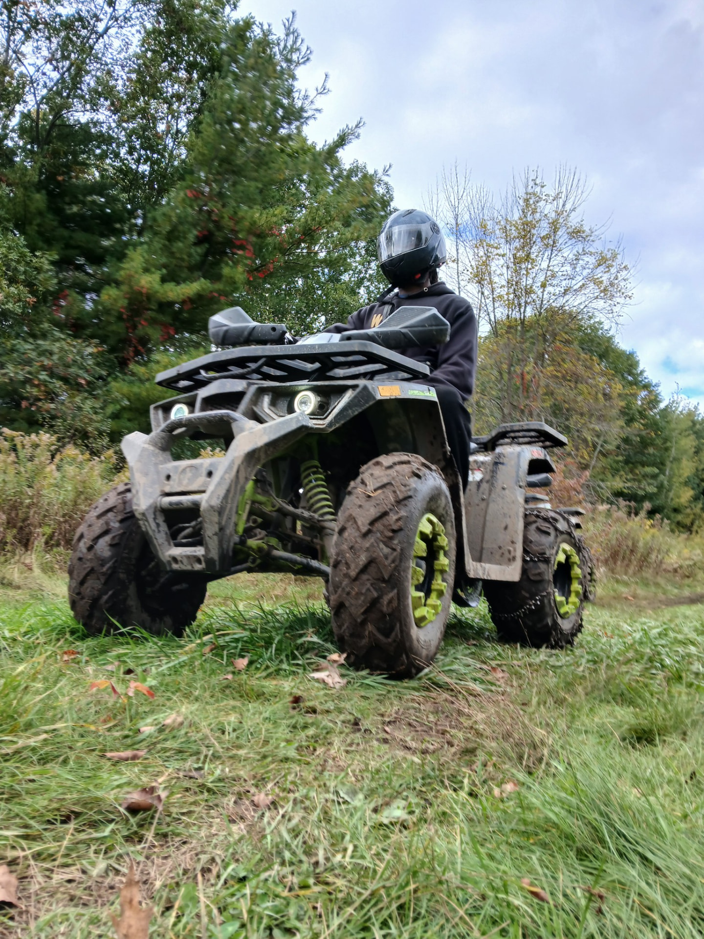 Mike in a helmet riding a mud-covered ATV across a grassy field
