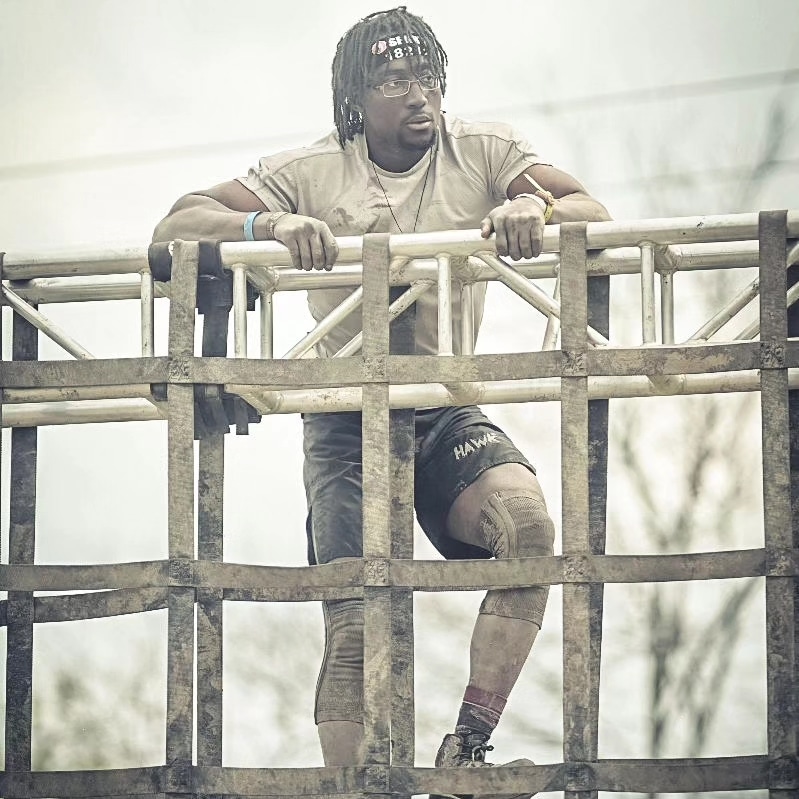 Mike climbing a rope net obstacle during a muddy race